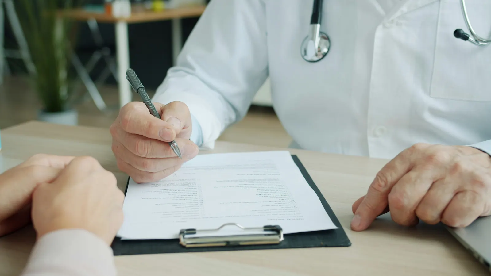 Doctor filling in a form on a clipboard during a consultation